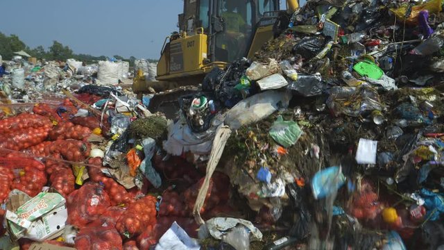 4K close-up view of a bulldozer that is pushing a pile of garbage over pockets of vegetables that have been dumped at a landfill dump site  