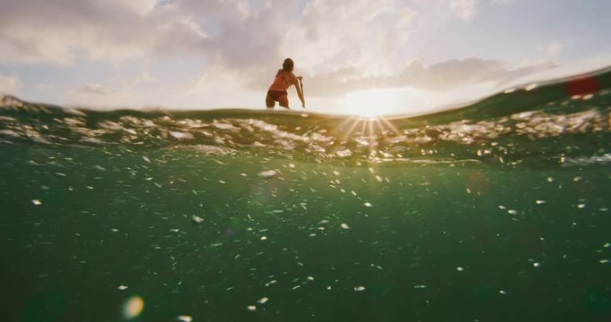 Over under shot of young happy active woman stand up paddling in the ocean at sunset, island ocean beach lifestyle, active healthy life