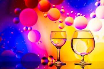 transparent glasses with water and oily drops on colorful background 