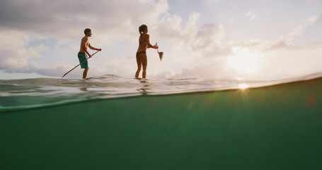 Over under shot of young happy active couple stand up paddling together at sunset in the ocean, island beach ocean lifestyle, active healthy life - Powered by Adobe