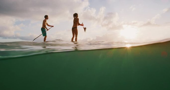 Over under shot of young happy active couple stand up paddling together at sunset in the ocean, island beach ocean lifestyle, active healthy life