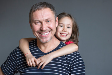 Little daughter hugs dad by the neck from behind