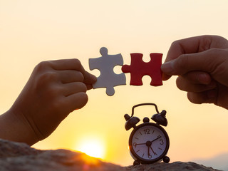 hands holding piece of jigsaw puzzle with clock on the stone at sunset nature background. teamwork concept