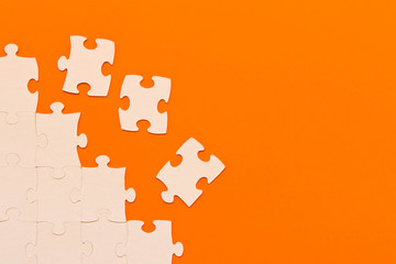 White jigsaw puzzles on orange background. The concept of development of thinking.