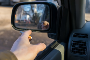 close up, the driver, the man holding a cigarette in his hand, sitting in the car, which is in the Parking lot