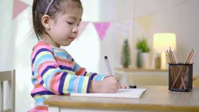 Kid's creativity, Child little asian girl writing in the book on the desk in the class room at home, Educational concept for school