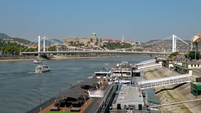 Sightseeing boats passing moored cruise ships on The Danube, Budapest, Hungary on a sunny day. Buda Castle and Fisherman's Bastion in the background.