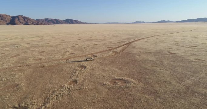 4K high tilt up aerial view of a 4x4 safari vehicle driving on a sand track through the African savannah grasslands with the famous fairy circles, Namibia