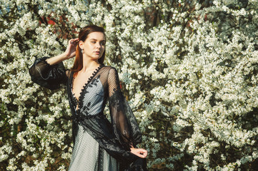 Obraz premium Portrait of a young beautiful fashionable woman in an evening dress . Girl posing in a blooming garden