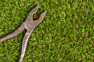Obraz premium Old rusty pliers lie on the green artificial grass