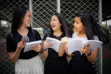 asian teenager holding school book and laughing with happiness emotion standing outdoor