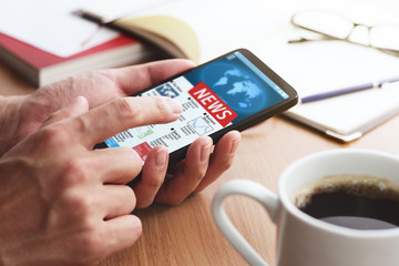 Closeup of male hands touching smartphone screen for reading news at table. Online news app on smartphone screen.