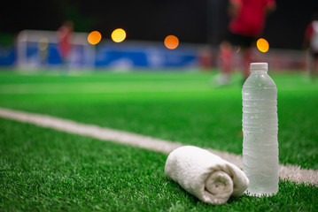 Water sport drink with towel blurred soccer background on green artificial grass at night.