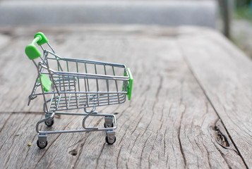 mini green shopping cart on wooden table with nature background