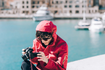 Female in red windbreaker jacket taking photo with camera at the sea. © Visual Intermezzo