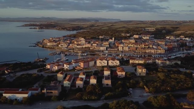 Aerial of a pretty village in Sardinia, Italy. Sunrise on the coast, parking yachts, mountains in the background