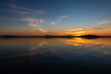 Obraz premium Symmetrcal, beautiful view of Trasimeno lake (Umbria, Italy) at sunset, with orange and blue tones in the sky