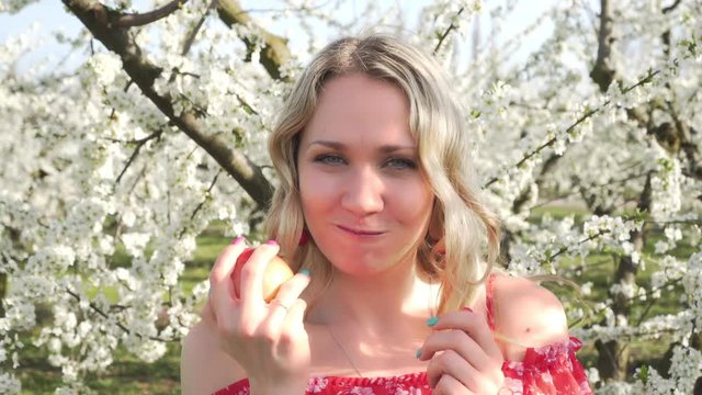 Young woman eats an apple on a background of flowering trees. Spring and nature.