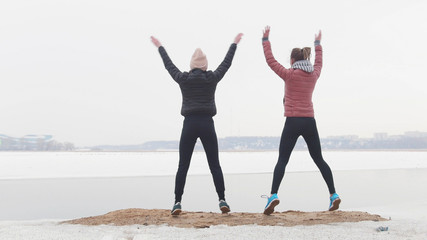 Outside training. Two slim women standing on the snowy beach and jumping.