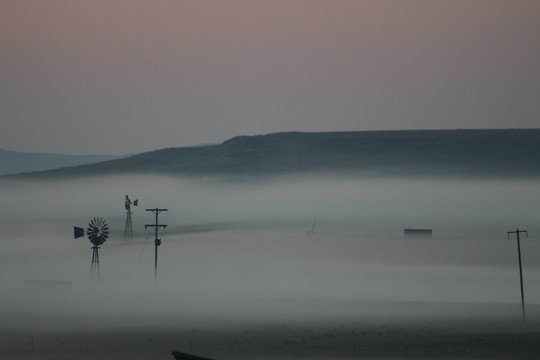 View of mountains and windmill on farm during early misty morning