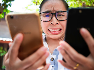 Business Asian young woman holding 2 smartphone do busy with work, Unhappy and worry face.