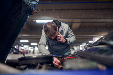 Brunet man talking on phone fixing car with open hood