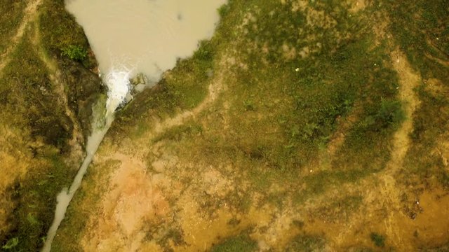 Top-view aerial passing over a lone motorcycle parked by a muddy stream and an abandoned canoe