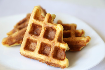 Belgian waffles in white plate. Healthy breakfast close up, pieces of freshly baked classic wafer