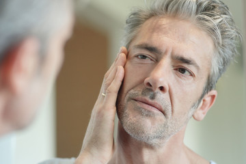 Obraz premium Portrait of mature handsome man looking in mirror at home