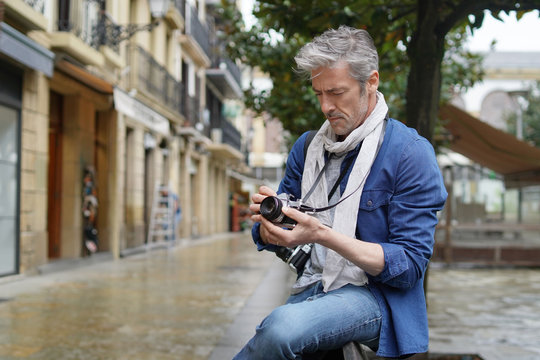 Mature photographer taking photos with vintage camera in European old town