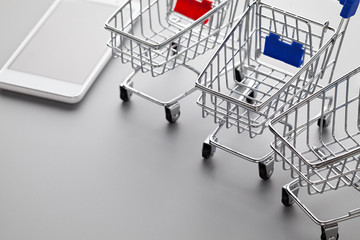 Three shopping carts and a mobile phone on a gray background