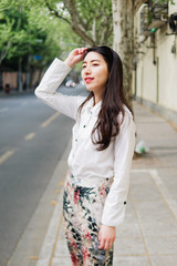 Outdoor portrait of young beautiful fashionable Chinese lady in casual clothes standing and smiling looking away in sunny Shanghai street. Female fashion. City lifestyle concept.