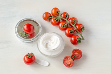 A small glass jar with a cosmetic face cream based on tomatoes on a light wooden background with copy space. Selective focus.