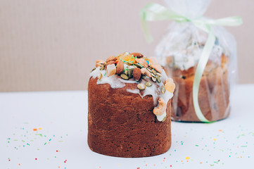 Selective focus close up image of delicious homemade Easter cakes freshly baked, one packed, multicolored sweet sprinkles, on white table. Easter, birthday greeting card or web banner concept
