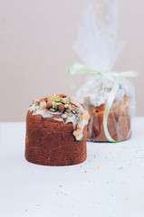 Selective focus close up image of delicious homemade Easter cakes freshly baked, multicolored sweet sprinkles, one packed, on white table. Easter, birthday greeting card or web banner concept