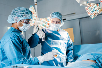 nurse and surgeon in uniforms and medical masks doing operation in operating room