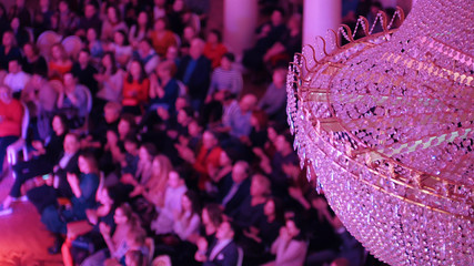Obraz premium A concert in the concert hall with a big crystal chandelier. People sitting on the chairs and clapping their hands