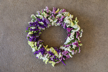 Handmade wreath decoration for the house door of limonium sinuatum or statice salem flowers in blue, lilac, violet, pink, white colors on a gray concrete background.