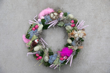 Easter holiday decor handmade wreath-stylish composition of spikelets of wheat, feathers, quail eggs for your home door decoration isolated on a gray concrete background.