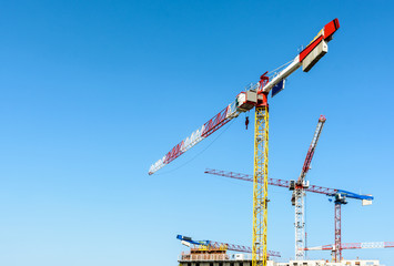 Low angle view of five large tower cranes above a concrete building under construction against blue...