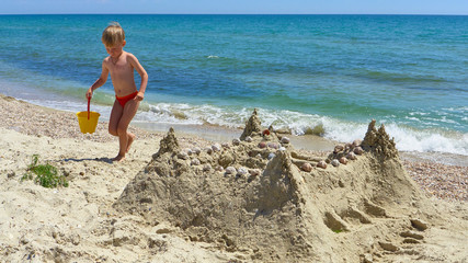 BOY WITH A BUCKET BUILDS A SAND LOCK ON THE BEACH OF THE BLACK SEA.