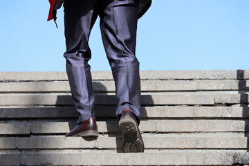 Man in a business suit climbing stairs to the blue sky, male feet in motion on the steps. Concept of career, success, official or businessman 