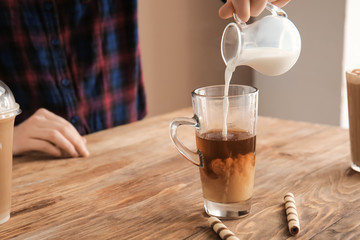 Woman preparing tasty frappe coffee on wooden table