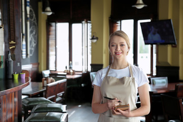 Young female waiter with notebook in restaurant