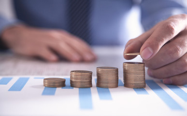 Businessman stacking coins with financial graphs on the desk.