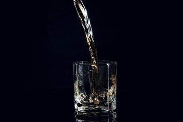 Whiskey pouring into glass with ice isolated on black background..