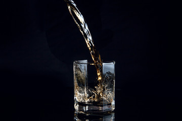 Whiskey pouring into glass with ice isolated on black background..