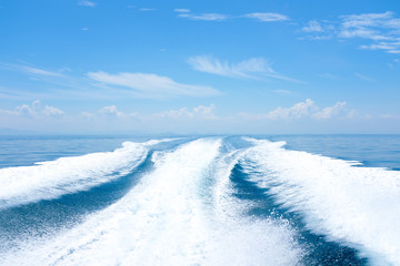 Sea wake trail behind a speed boat with waves, foam, bubbles on the ocean water surface with clear bright blue sky. Travel in tropical summer season concept. 