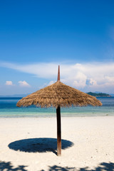 Natural palm leaves umbrella on white sand beach and bright blue sea water in background under crystal clear bright blue sky in sunny day. Tropical summer season vacation travel.
