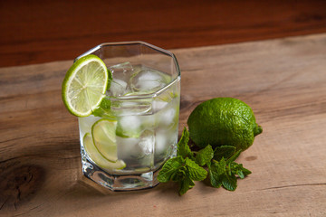 Summer cocktail mojito in glass, sliced lime and mint on wooden background..